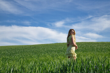 Young, beautiful, blonde woman in a yellow dress, walking through a green wheat field, alone, quiet and peaceful. Concept beauty, relaxation, tranquility, calm, fields, meadows.