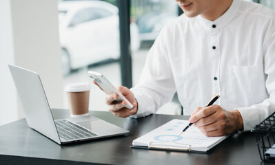Young handsome man typing on tablet and laptop while sitting at the working wooden table office