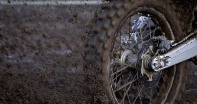 Slow motion macro of dirt splashing from motorbike rear wheel while rider is in action in motocross race.