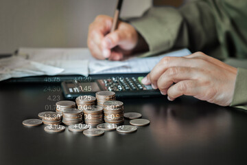 Accountant working on desk using calculator with coins placed next to the concept of calculating financial reports, calculating taxes, income and expenses Calculate numbers for your organization