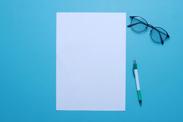 Top view of white blank paper for mockup with eyeglasses and pen over blue background