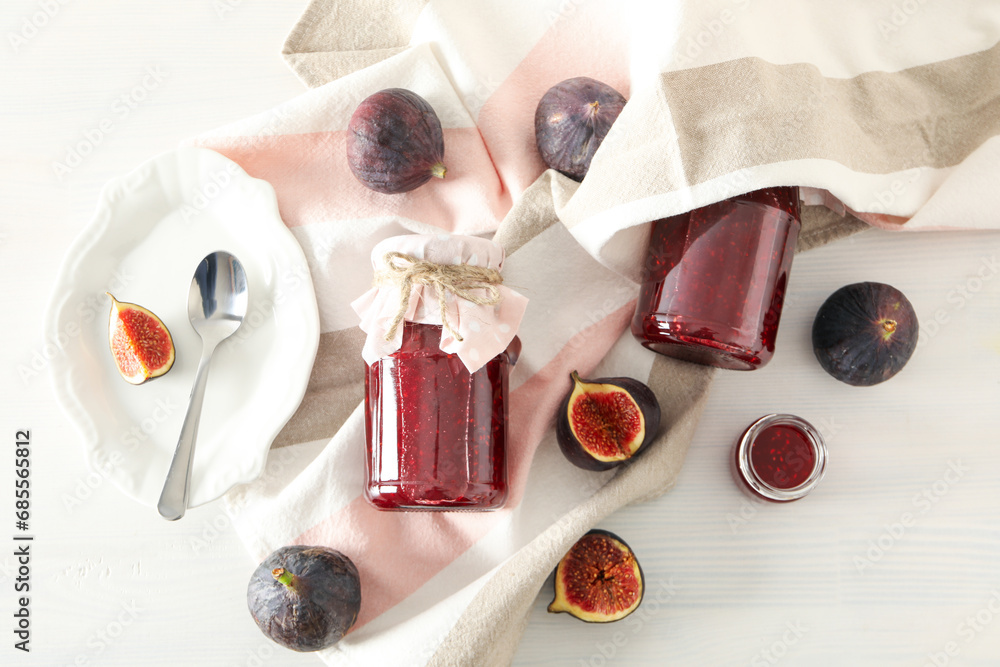 Sticker figs, jars of jam and towel on light background, top view