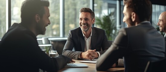 Two good looking businessmen are happily discussing a project in a conference hall One shares ideas with enthusiasm and the other listens attentively They sit at a desk and smile copy space image - obrazy, fototapety, plakaty