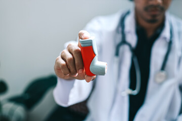 Male doctor holding and showing asthma inhaler. Medical portable equipment for asthma attack.  - obrazy, fototapety, plakaty