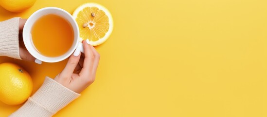 Top view photo of hands in yellow sweater holding cup of tea with lemon and smartphone on light orange background copy space image
