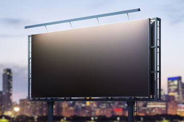 Blank black billboard on cityscape background at evening, perspective view. Mock up, advertising concept