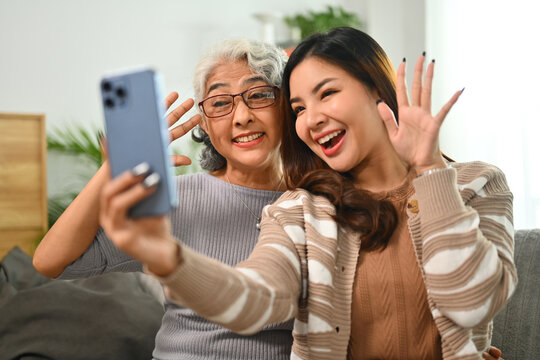 Cheerful young Asian woman taking selfie picture on smartphone with happy mature mother