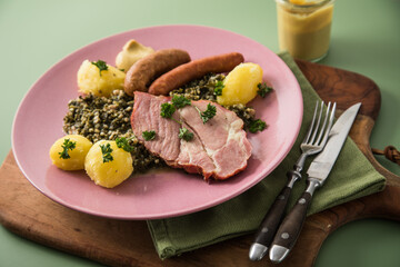 Oldenburger Grünkohl mit geräucherter Kohlwurst, Pinkel, Kassler Nacken, Kartoffeln, Senf, Petersilie auf Holzbrett, Serviette, Teller pink, und grün Hintergrund