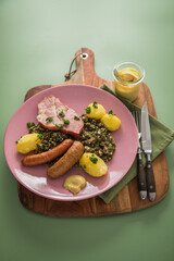 Oldenburger Grünkohl mit geräucherter Kohlwurst, Pinkel, Kassler Nacken, Kartoffeln, Senf, Petersilie auf Holzbrett, Serviette, Teller pink, und grün Hintergrund