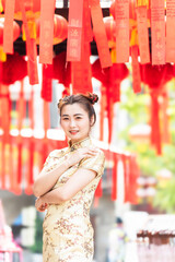 Asian woman wearing traditional cheongsam qipao dress with gesture of congratulation in Chinese Buddhist temple. Emotion smile new year concept