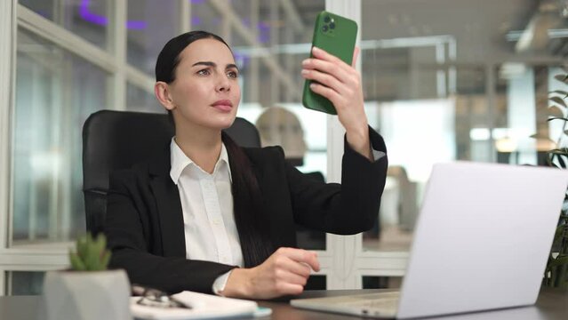 Serious business woman working with modern laptop and holding smartphone in hand while trying to catch connection in office. Caucasian lady looking for mobile internet to sending message online.