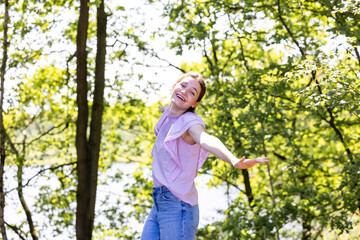 The image features a young woman with a playful pose, her arms outstretched, dancing or twirling in a forest setting. Her carefree spirit is infectious, and her smile is as bright as the dappled