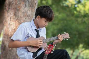 Asian cute boy playing acoustic guitar in the park.