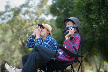 Asian boys holding binoculars and watching birds which fying on sky, insects, forest animals and living things which crawling and jumping on the branches and on the underside of trees in tropical park