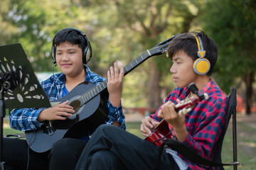 Asian cute boys doing summer activity at their front yard by playing and showing acoustic guitars,...