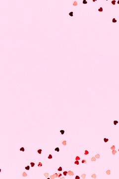 Metallic red confetti in a heart shape on a pink background. Place for text.