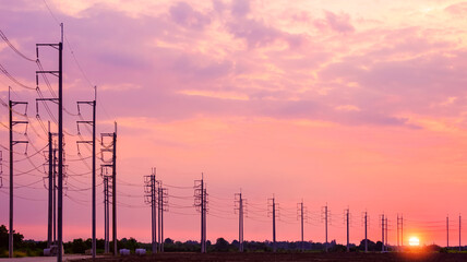 Silhouette row of electric poles with cable lines on curve street in countryside area against...
