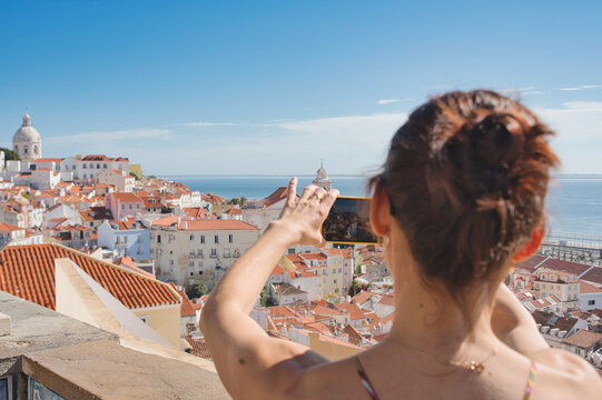 A tourist woman takes photos of the beautiful cityscape of Lisbon, with the colorful houses and roofs at the Alfama district, Portugal
