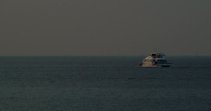 A medium-sized ship sails on the water at sunset, silhouettes of boats and sailing ships in the distance