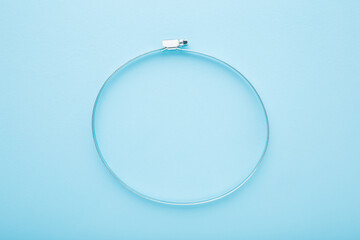 New metal hose clamp on light blue table background. Pastel color. Closeup. Top down view.