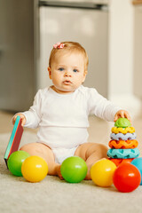Obraz premium Vertical photo of baby girl sitting on floor with some toys.