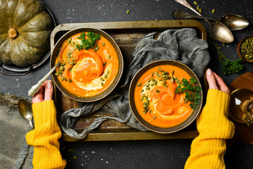 Two bowls of pumpkin porridge or cream soup with pumpkin seeds and cream. Autumn food concept. Top...