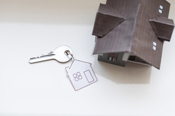 Keys with trinket in shape of house on white background, top view. Real estate agent services
