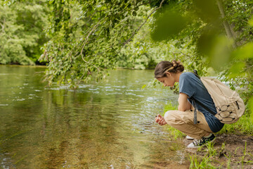 female tourist on the bank of a forest river, enjoying nature