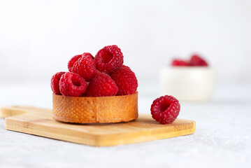 Tartlet with raw raspberries and cream, fresh dessert for breakfast on a wooden board.