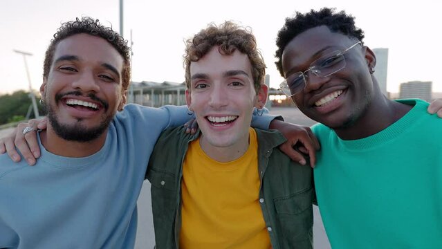 Portrait of three young diverse male friends laughing at camera outdoors. Multiracial men friends having fun together enjoying life moments at city street. Youth community and friendship concept.