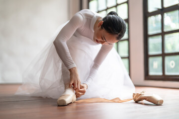 Ballerina in ballet shoes. Asian girl tying ribbons of toe shoes. ballet dancer preparing and wearing ballet shoes in dance studio prepares for a rehearsal.