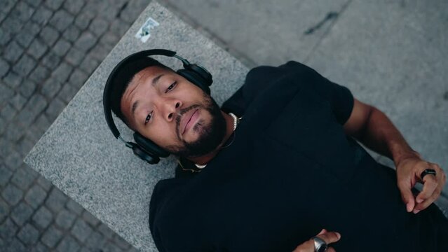 Top view, relaxed music lover with closed eyes lying back in urban setting while streaming a new album release and appreciating every beat with high-quality sound in noice cancelation headphones