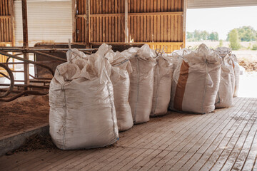 A row of large, filled industrial feed bags neatly aligned inside a rustic farm storage barn