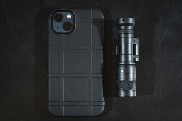 A modern phone with two cameras in a rubber protective case and a tactical flashlight.