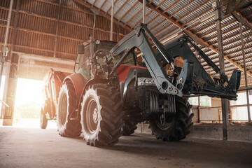 A red and black modern tractor equipped with a loader, parked inside a spacious wooden barn