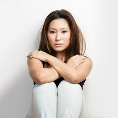 Cool Asian woman sitting in front of a white wall.