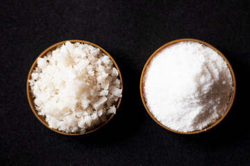 Coarse and fine natural sea salt in plastic bowl isolated on black background, top view, flat lay.