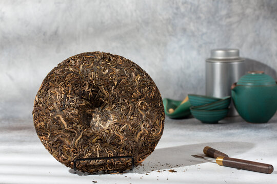 Round flat disc of puer tea with puerh tea awl on gray background. Pressed Chinese fermented Pu-erh tea.