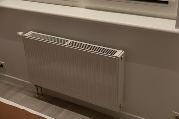 A steel panel heating radiator is placed under the windowsill on a white wall.