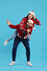 Happy young couple in Christmas sweaters and Santa hats on light blue background