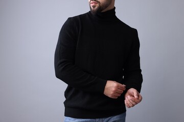 Obraz na płótnie Canvas Man in stylish black sweater on grey background, closeup