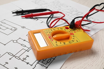 Wiring diagrams and digital multimeter on white wooden table, closeup