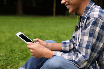 Student studying with tablet on green grass in park, closeup