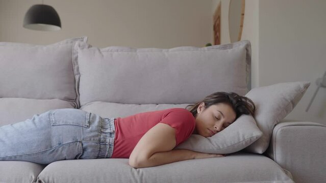 Exhausted or bored young sleepy woman falls down on sofa. Apathetic tired lazy lady sleeping on couch at home alone. Funny girl lying asleep feeling lack of motivation, fatigue or depression concept
