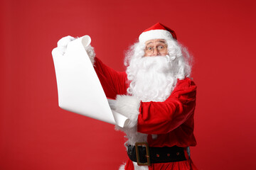 Merry Christmas. Santa Claus holding wishlist on red background
