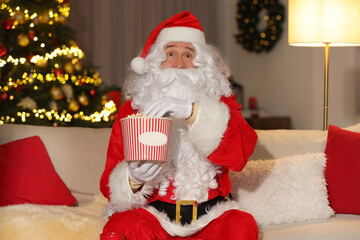 Merry Christmas. Santa Claus with popcorn bucket watching TV on sofa at home