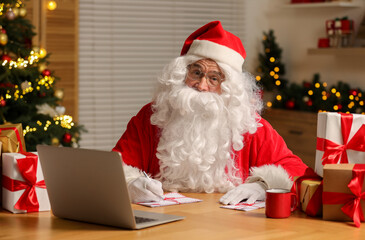 Santa Claus signing Christmas letters at table in room