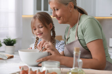 Happy grandmother with her granddaughter cooking together in kitchen