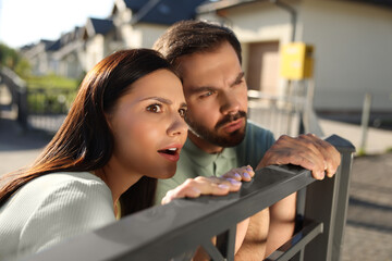 Concept of private life. Curious couple spying on neighbours over fence outdoors
