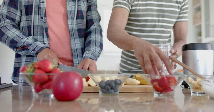 Happy diverse gay male couple preparing healthy fruit smoothie in kitchen, slow motion